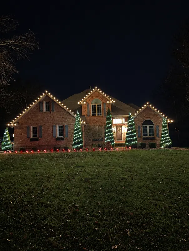 Brick home with warm white roofline lights and green light cones in front